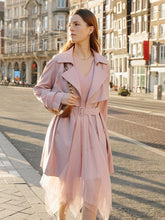 A lady wears a trench coat and a pink skirt.